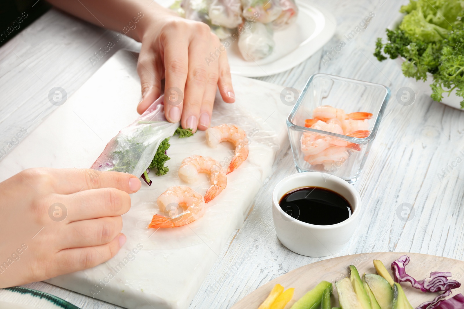 Photo of Woman making rice paper roll at white wooden table, closeup