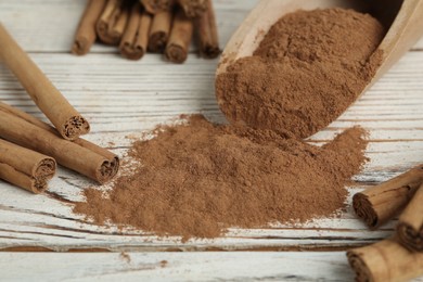 Photo of Aromatic cinnamon powder and sticks on white wooden table, closeup