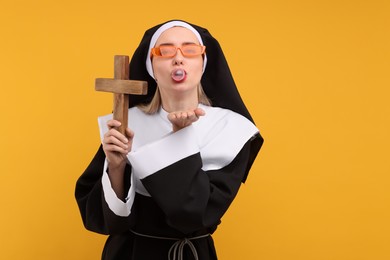 Woman in nun habit blowing bubble gum against orange background. Space for text