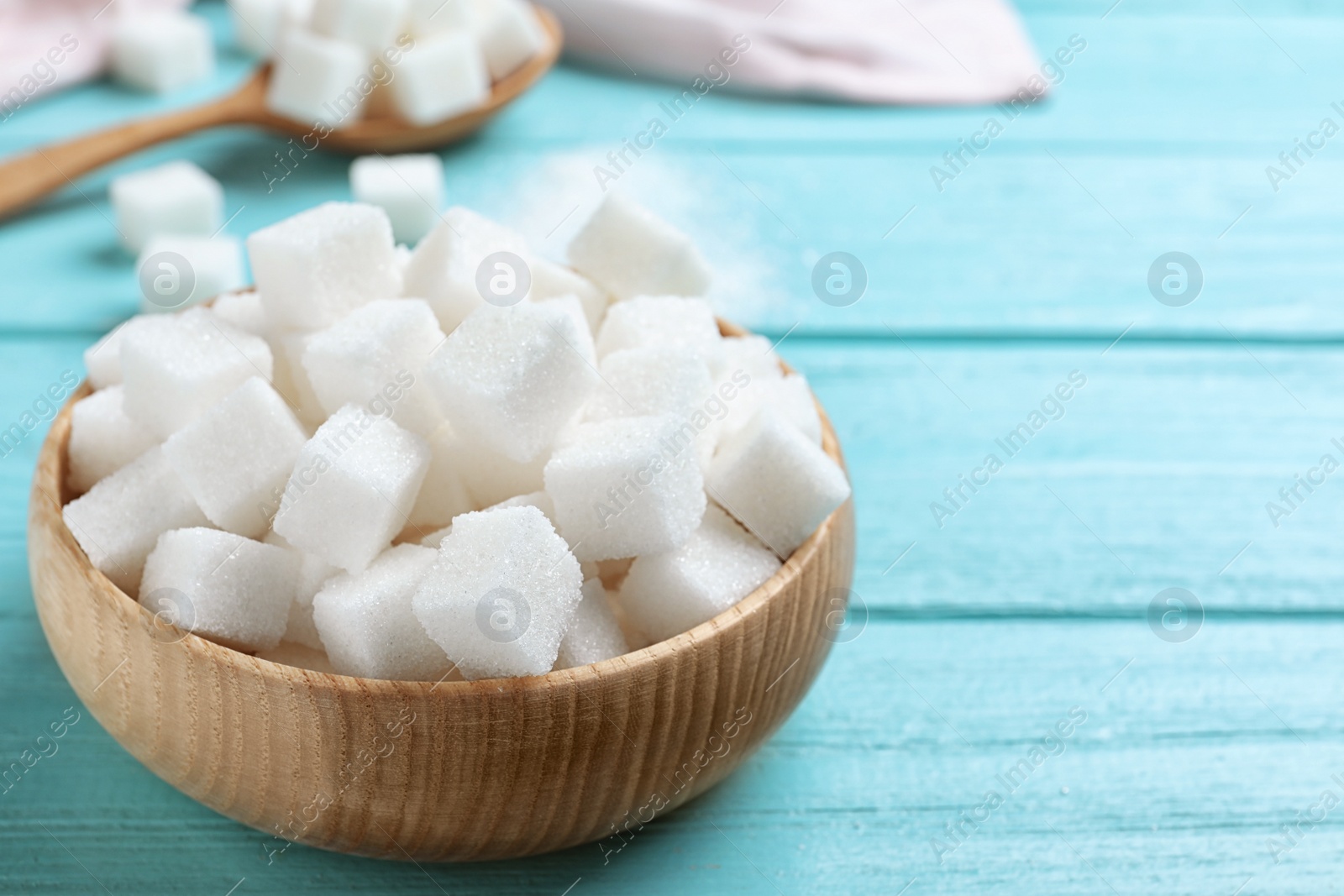 Photo of Refined sugar cubes in bowl on blue wooden table