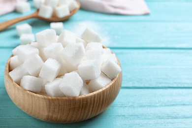 Photo of Refined sugar cubes in bowl on blue wooden table