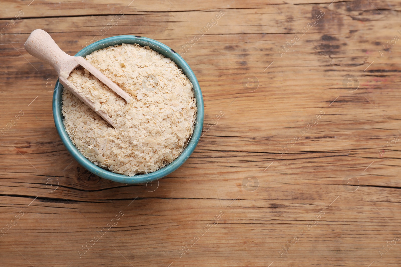 Photo of Scoop and bowl of brewer`s yeast flakes on wooden table, top view. Space for text