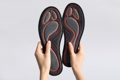 Photo of Woman holding pair of orthopedic insoles on light gray background, closeup