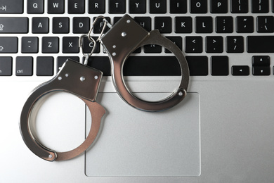 Photo of Handcuffs on modern laptop, top view. Cyber crime