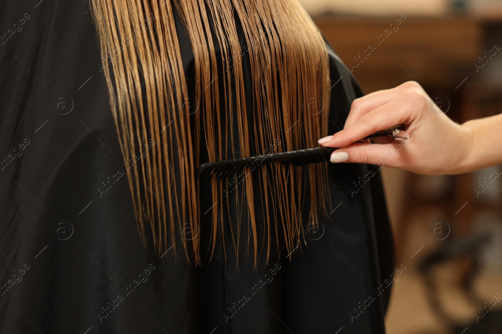 Photo of Professional hairdresser combing girl's hair in beauty salon, closeup