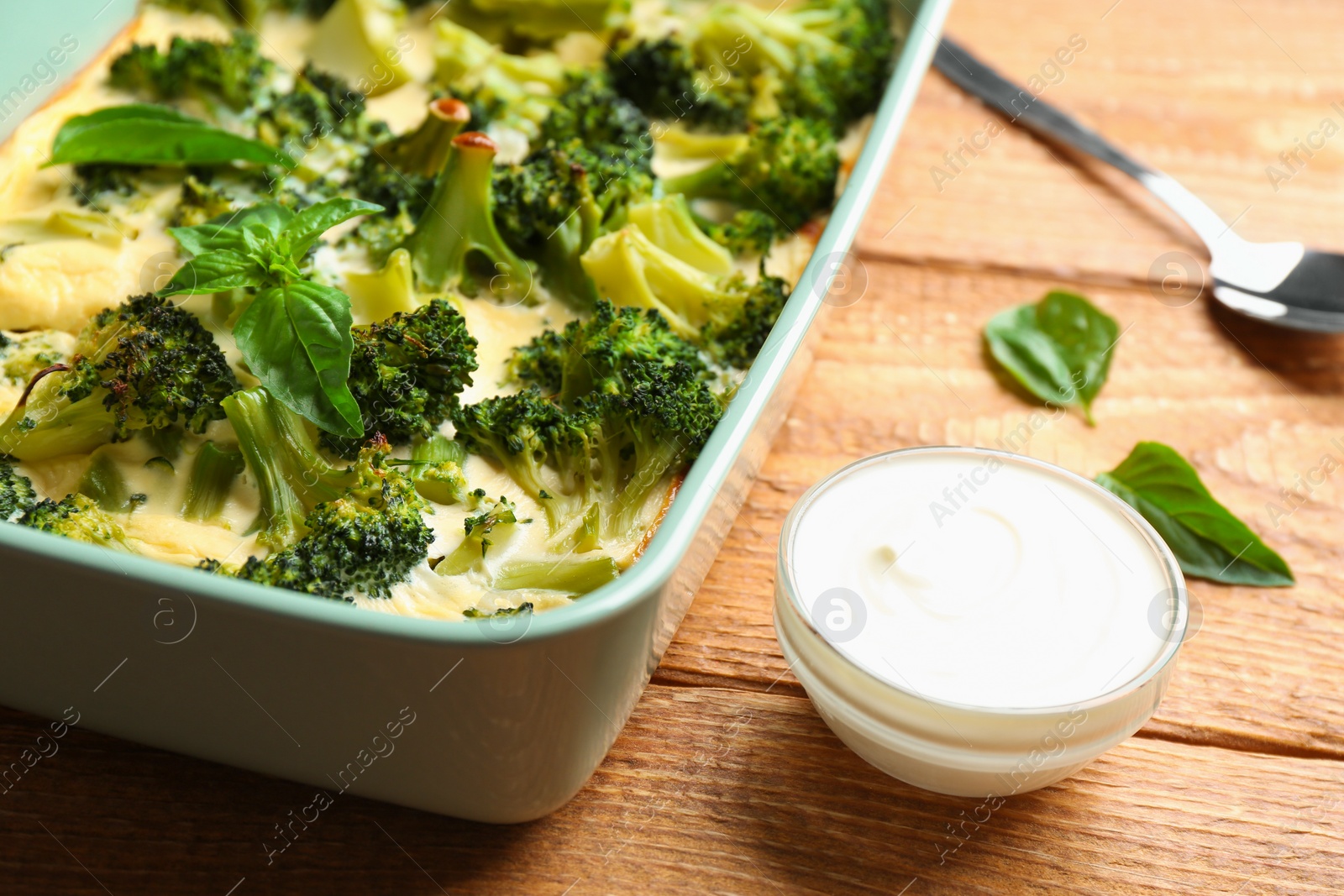 Photo of Tasty broccoli casserole served with sour cream on wooden table