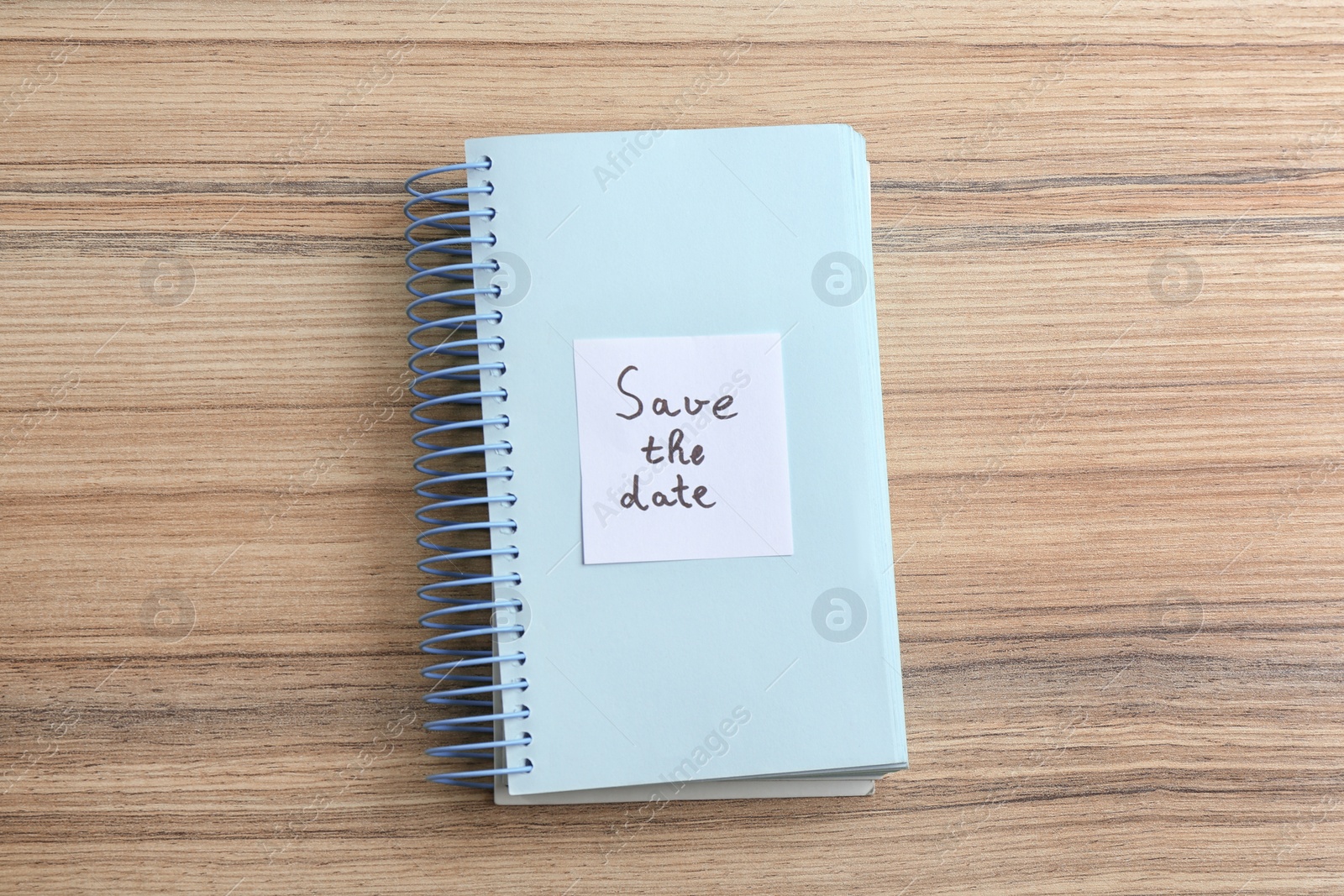 Photo of Notebook with phrase SAVE THE DATE on wooden table, top view