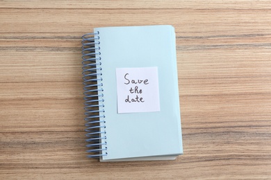 Notebook with phrase SAVE THE DATE on wooden table, top view