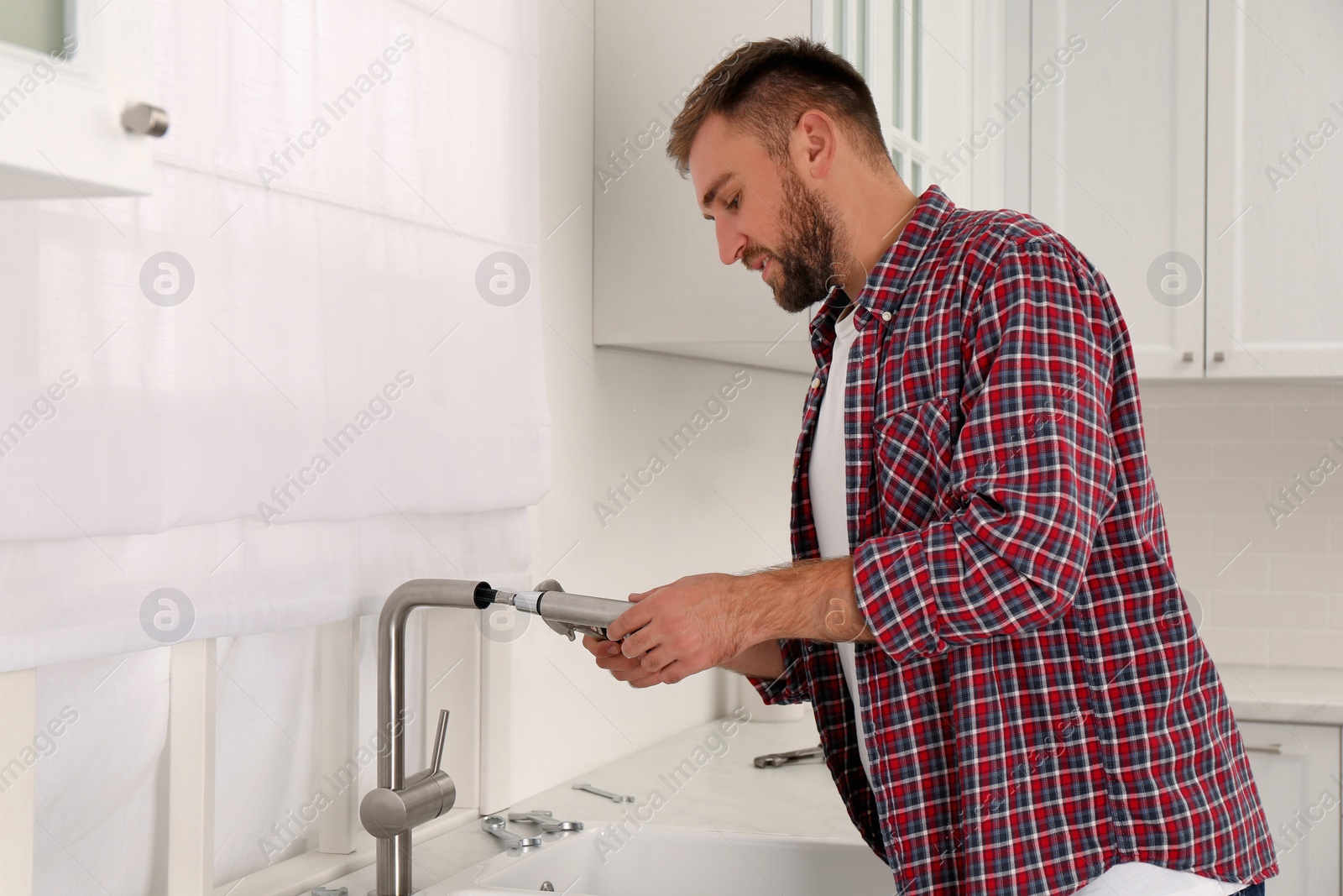 Photo of Man repairing water tap with wrench in kitchen