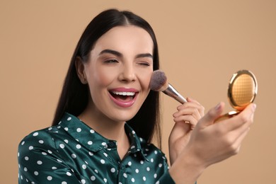 Photo of Happy woman with cosmetic pocket mirror applying makeup on light brown background