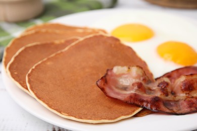 Photo of Tasty pancakes with fried eggs and bacon on white wooden table, closeup