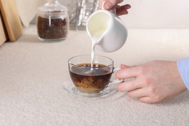 Photo of Woman pouring milk into cup with aromatic coffee at light textured table, closeup