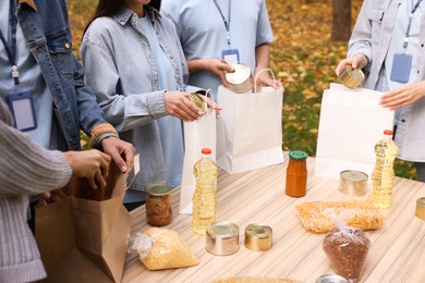 Photo of Volunteers packing food products at table in park, closeup