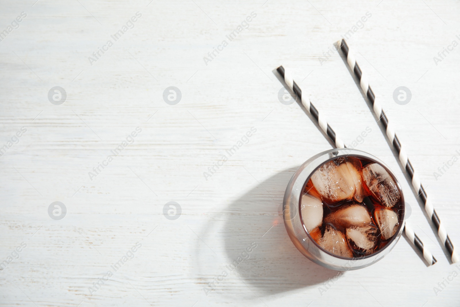 Photo of Glass of refreshing cola with ice cubes on white wooden background, top view. Space for text