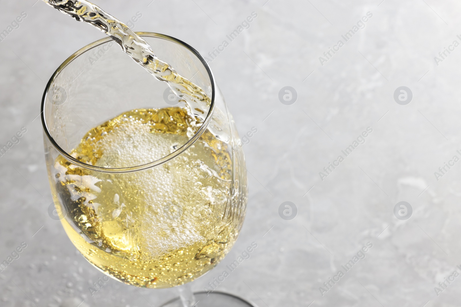 Photo of Pouring tasty aromatic wine in glass at gray marble table, closeup. Space for text