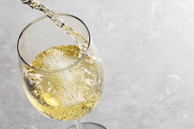 Pouring tasty aromatic wine in glass at gray marble table, closeup. Space for text