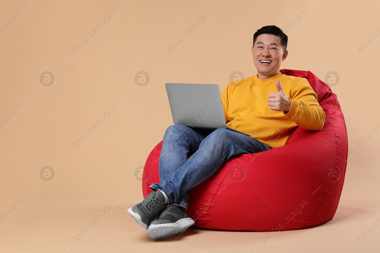 Photo of Emotional man with laptop showing thumb up gesture on beige background, space for text