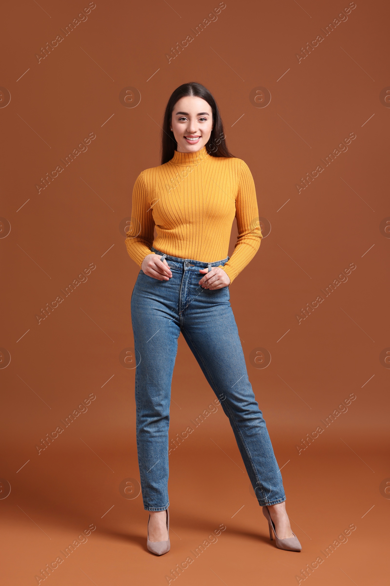 Photo of Young woman in stylish jeans on brown background