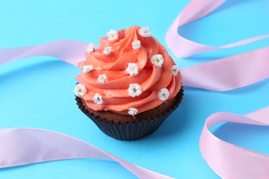 Photo of Delicious cupcake with bright cream and flowers on light blue background