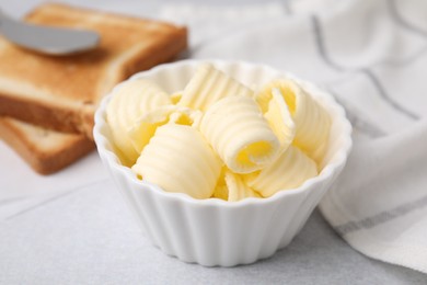 Photo of Tasty butter curls in bowl and toasts on light grey table, closeup