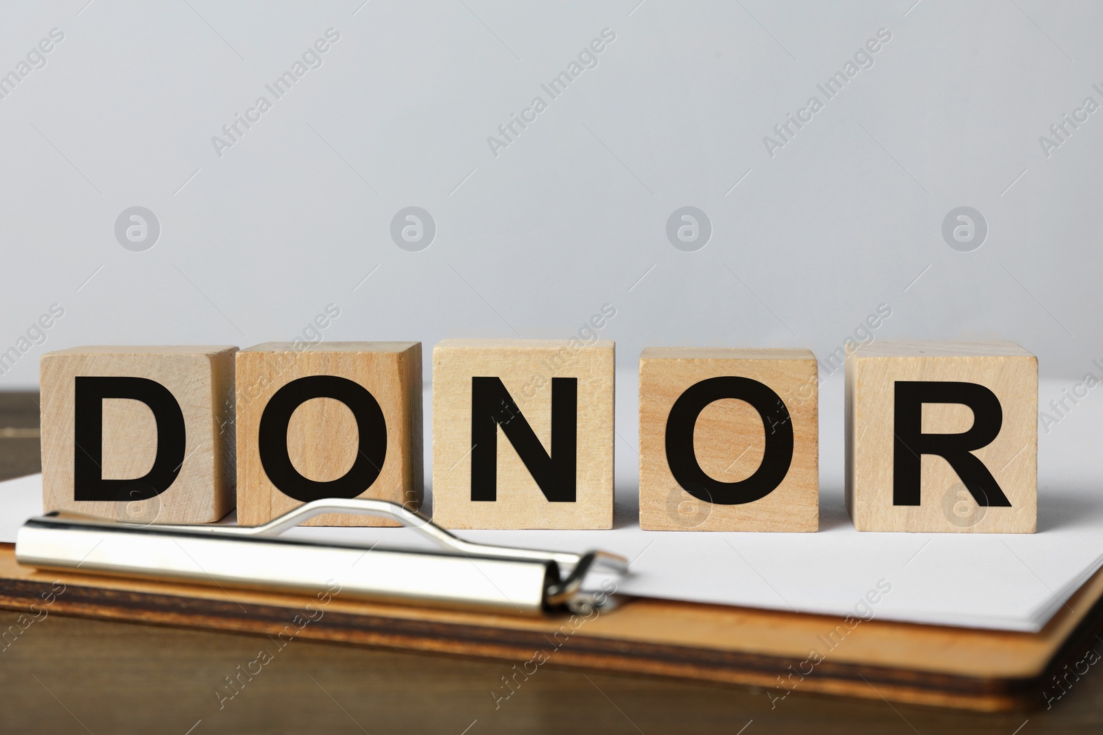 Photo of Word Donor made of cubes and clipboard on wooden table, closeup