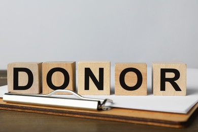 Word Donor made of cubes and clipboard on wooden table, closeup