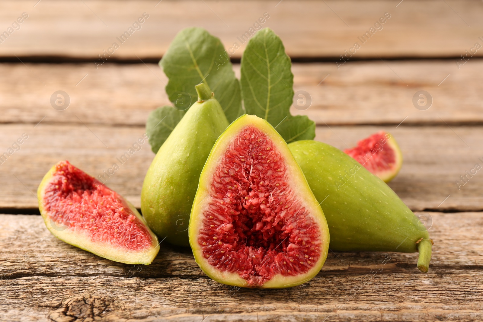 Photo of Cut and whole green figs on wooden table, closeup