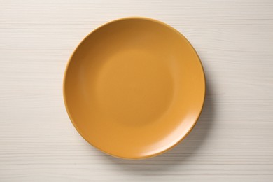 Photo of One orange ceramic plate on white wooden table, top view