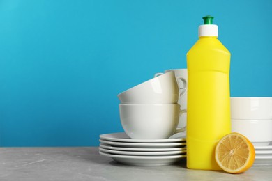 Photo of Clean tableware, dish detergent and lemon on grey table against light blue background. Space for text