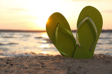 Photo of Stylish flip flops on sand near sea, space for text. Beach accessories