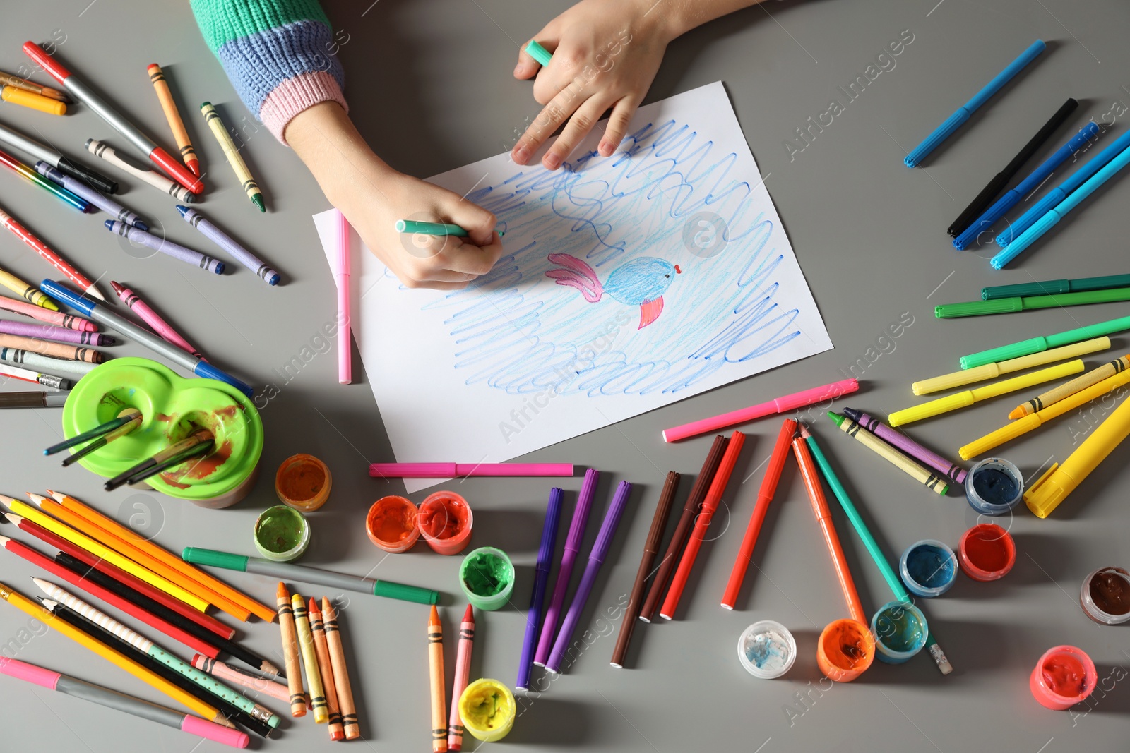 Photo of Little girl painting picture at table with painting tools indoors, top view