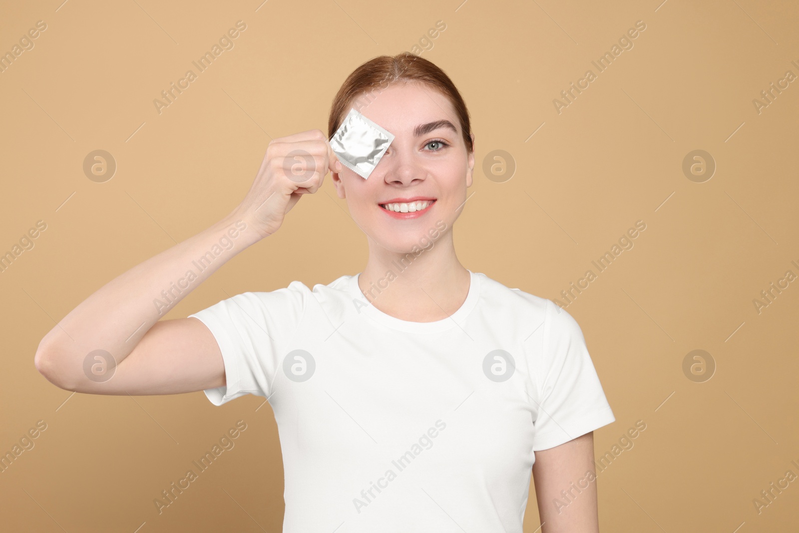 Photo of Woman holding condom on beige background. Safe sex