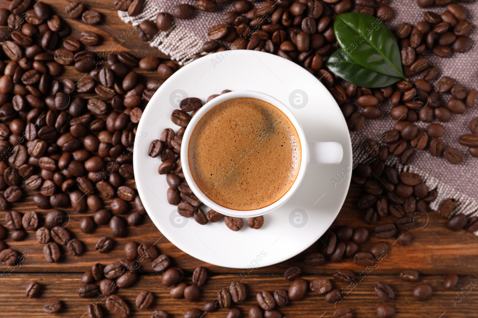 Photo of Cup of hot aromatic coffee and roasted beans on wooden table, flat lay