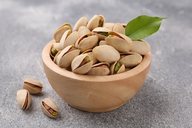 Delicious pistachios in bowl on grey textured table