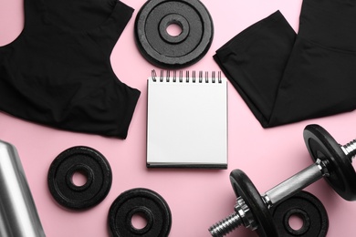 Photo of Flat lay composition with sportswear, notebook and dumbbell on pink background, space for text. Gym workout plan