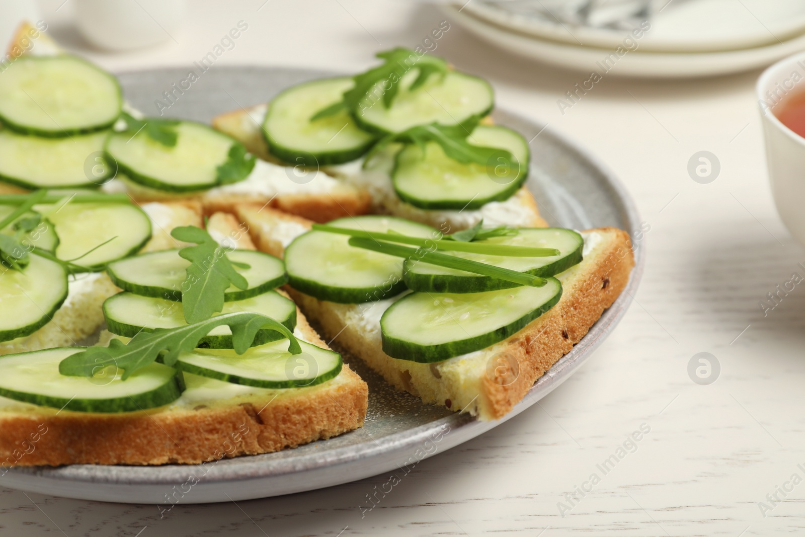 Photo of Plate with traditional English cucumber sandwiches on white wooden table, closeup