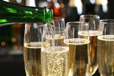 Pouring champagne into glasses on blurred background, closeup