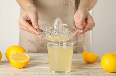 Photo of Woman pouring freshly squeezed lemon juice in glass at white wooden table, closeup