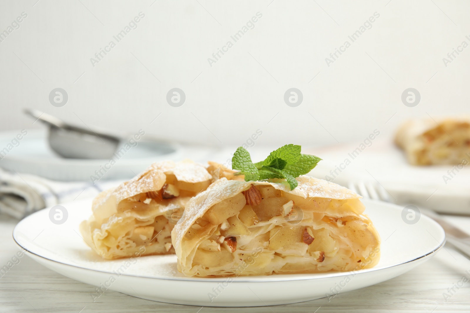 Photo of Pieces of delicious apple strudel with almonds, powdered sugar and mint on white wooden table, closeup