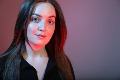 Photo of Portrait of beautiful young woman on color background with neon lights. Space for text