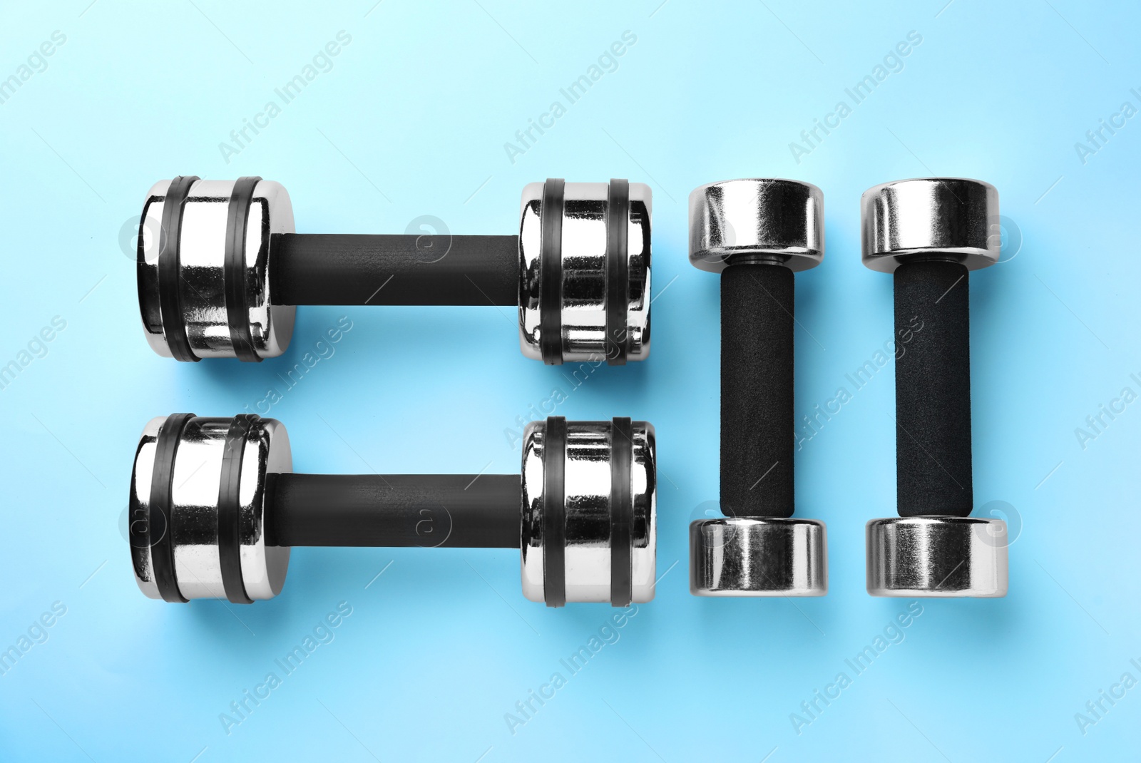 Photo of Many stylish dumbbells on light blue background, flat lay