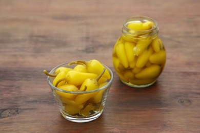 Photo of Glass jar and bowl of pickled yellow jalapeno peppers on wooden table