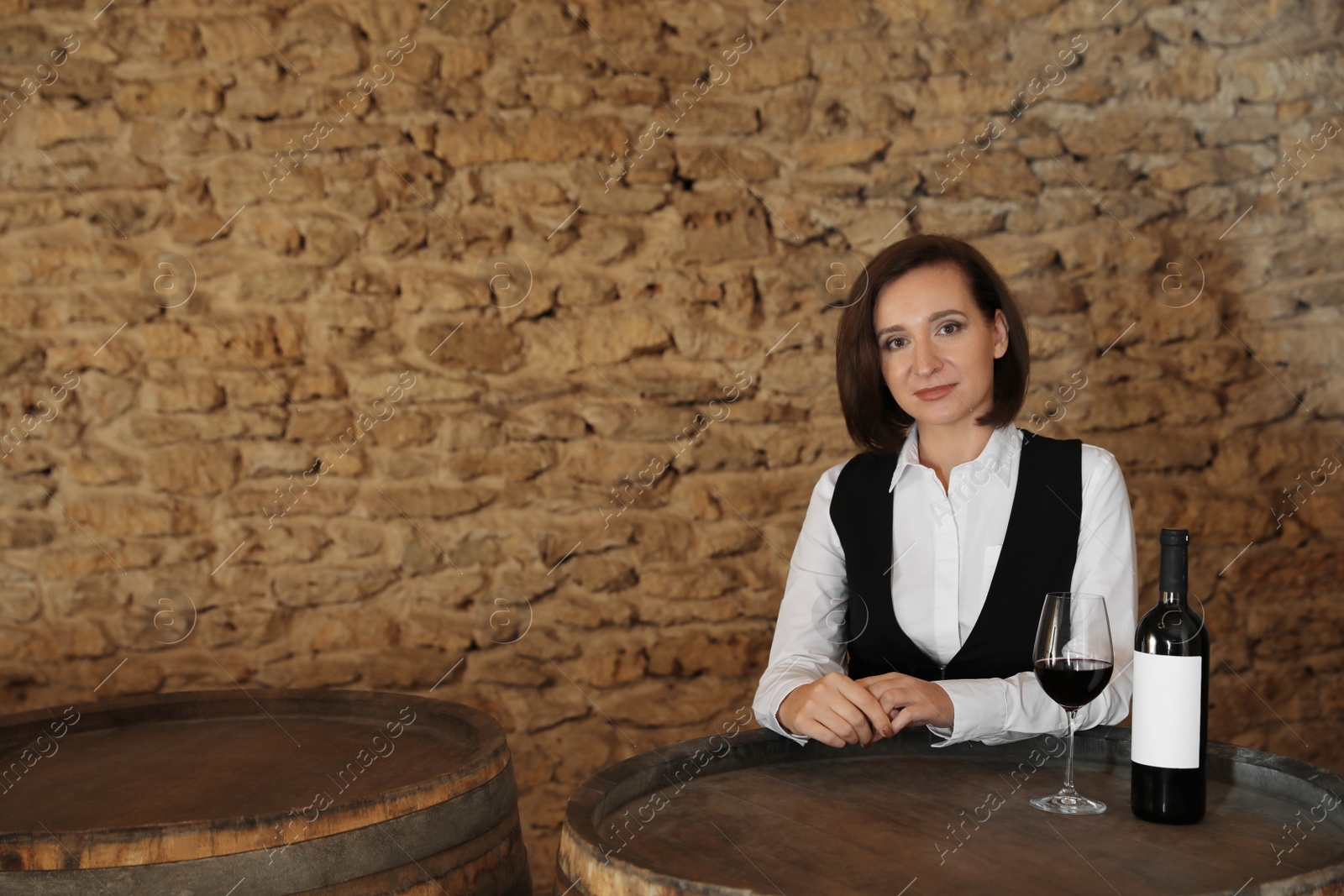 Photo of Female sommelier with glass and bottle of red wine at table indoors