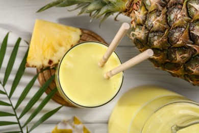 Tasty pineapple smoothie and fruit on white wooden table, flat lay