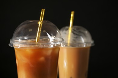 Photo of Refreshing iced coffee with milk in takeaway cups on black background, closeup