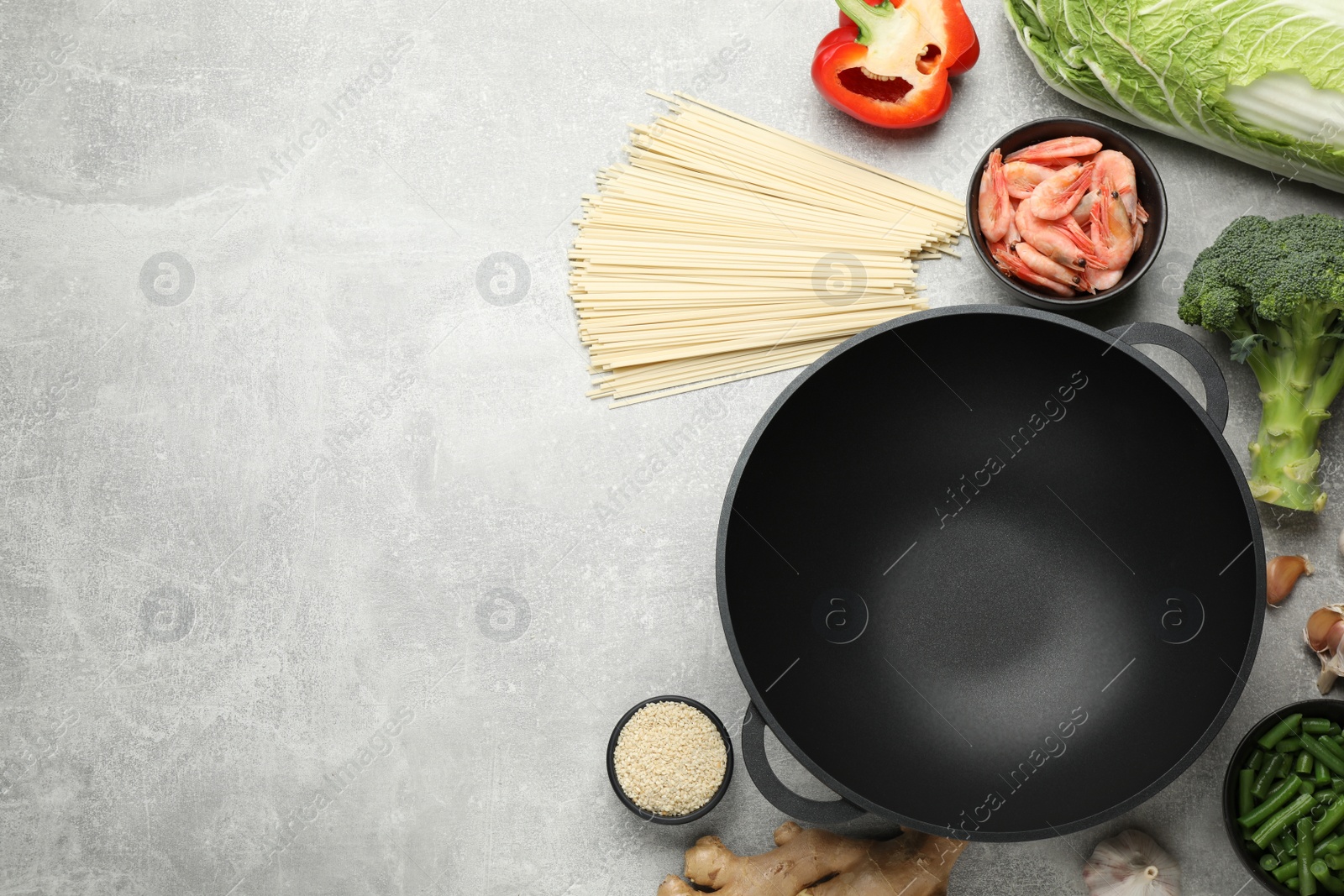 Photo of Empty iron wok and raw ingredients on light grey table, flat lay. Space for text