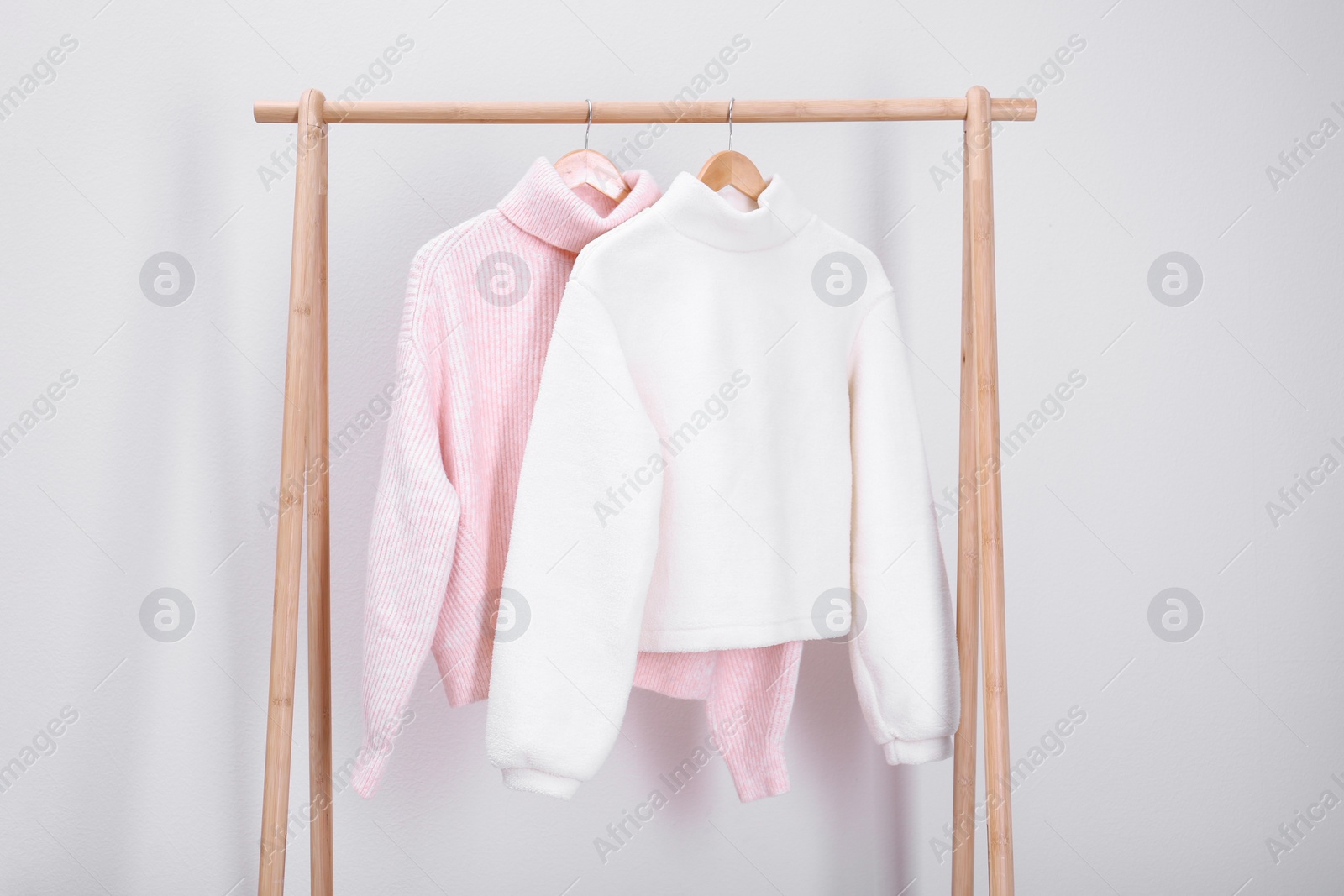 Photo of Stylish knitted sweaters hanging on clothing rack near light wall