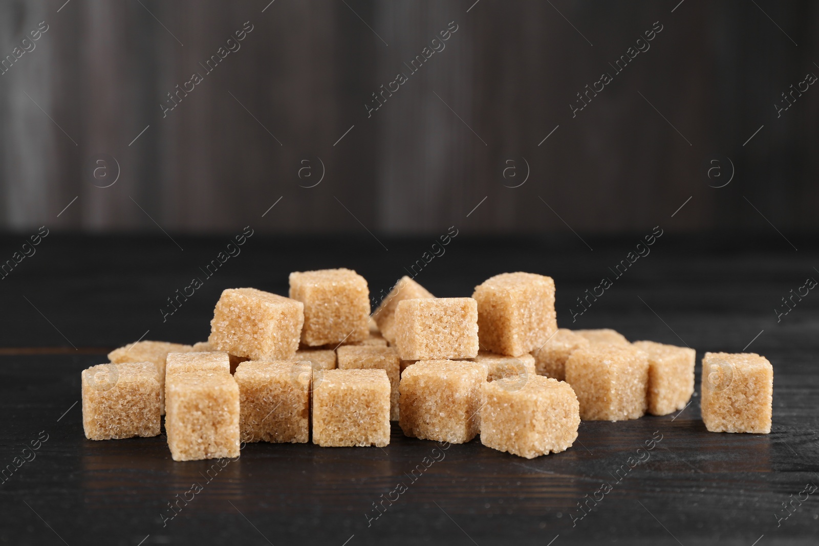 Photo of Many brown sugar cubes on black wooden table, closeup