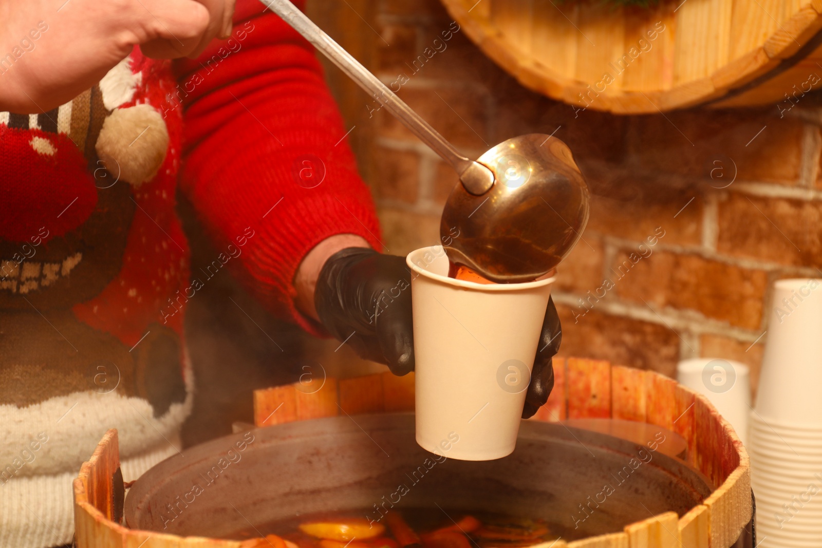 Photo of Seller pouring tasty aromatic mulled wine into cup at winter fair, closeup