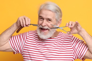Photo of Senior man with mustache holding scissors and blade on orange background